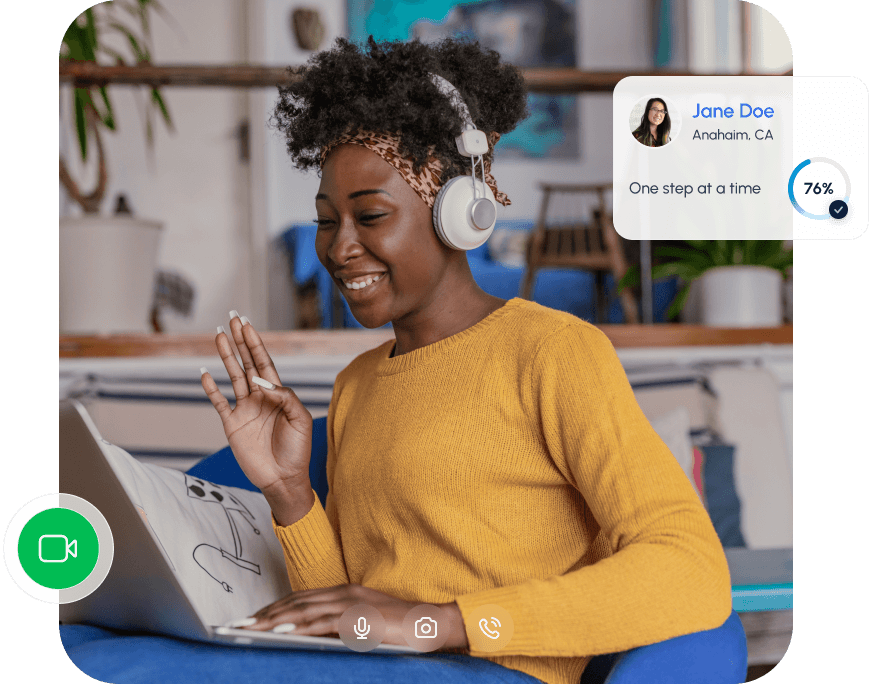 Smiling woman on a video call using a laptop and headphones, waving during an online session.