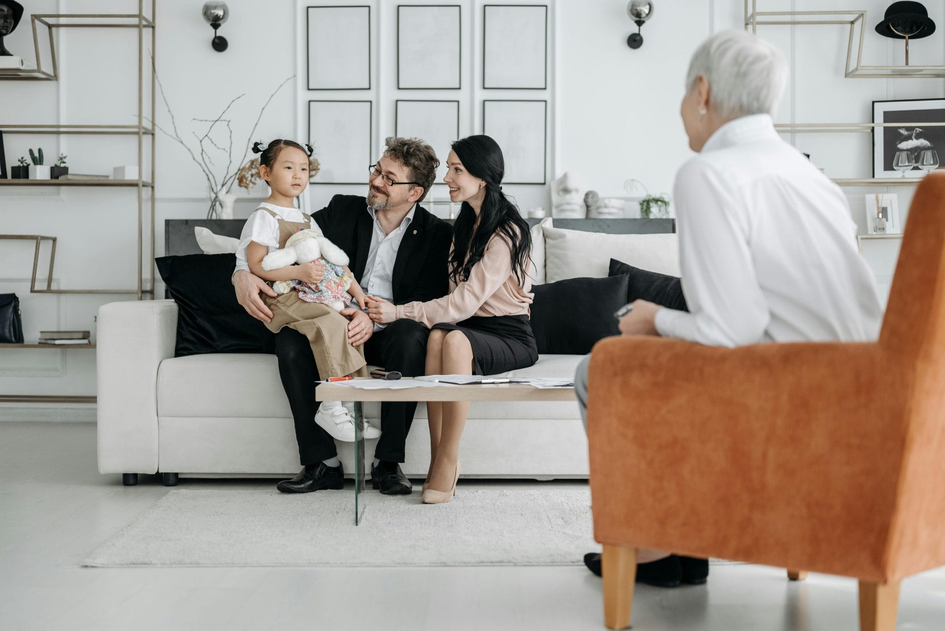 Family sitting with a young child during a counseling session while a therapist takes notes nearby.