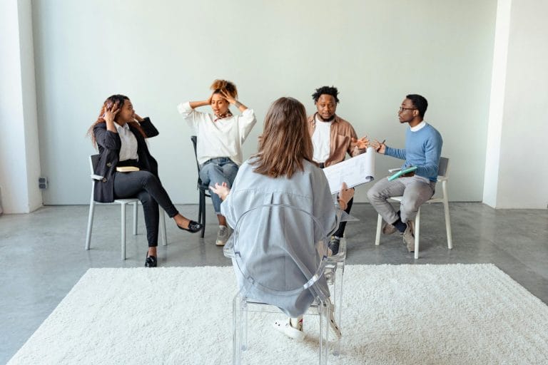 Group therapy session with participants discussing emotions while a therapist facilitates the conversation.