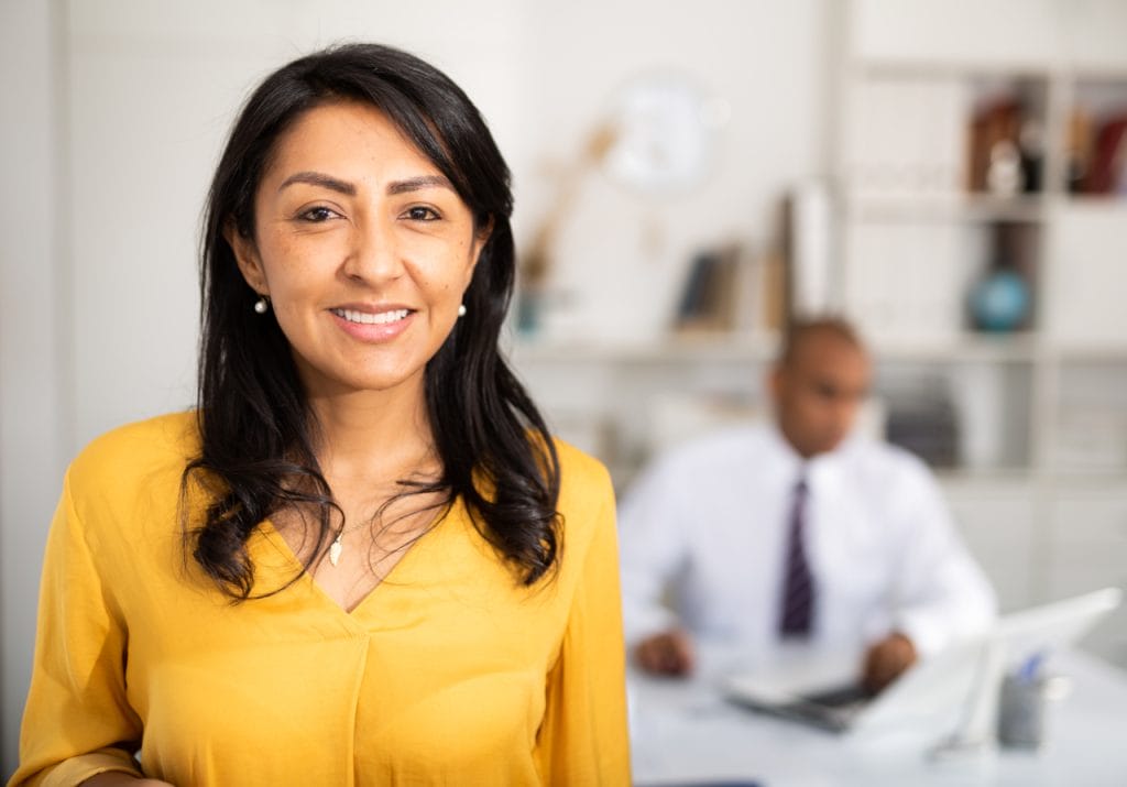 Confident businesswoman smiling in a modern office setting, representing professional consulting and client-focused service.